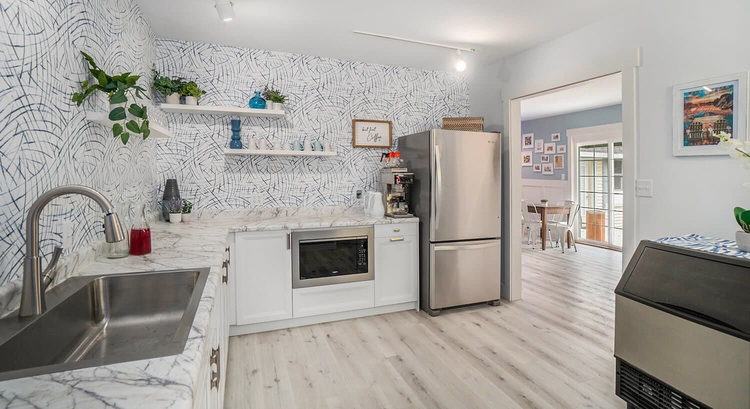 Modern kitchen featuring white cabinets, marble countertops, and patterned wallpaper.